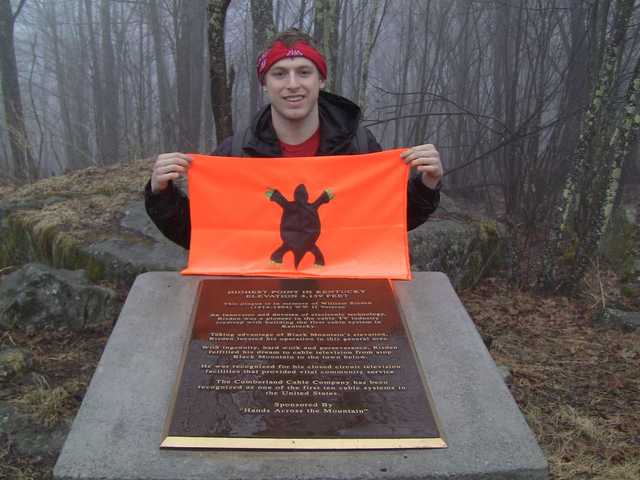 Summit plaque on a foggy Black Mountain, flag held just above it