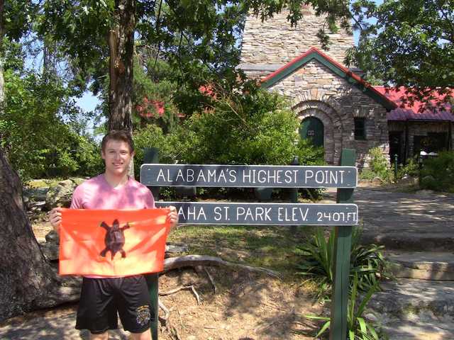 Alabama's Highest Point sign with the stone summit tower of Cheaha Mountain behind