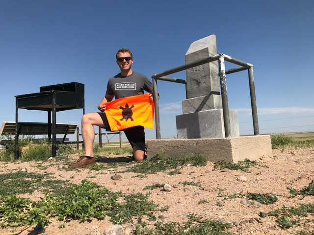 Panorama Point monument on the open plains, Justin kneeling beside it