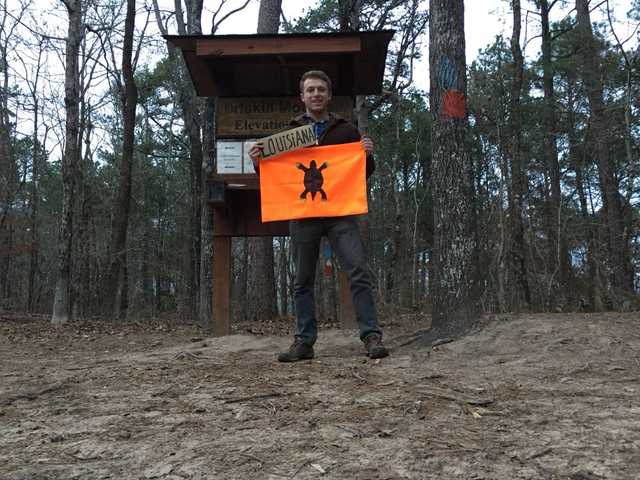 Trail kiosk on wooded Driskill Mountain, Justin also holding a Louisiana sign